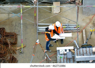 Candid aerial view of two unrecognized civil engineers wearing white safety helmets and orange color vasts inspecting construction site. Building development concept. Real people. Copy space