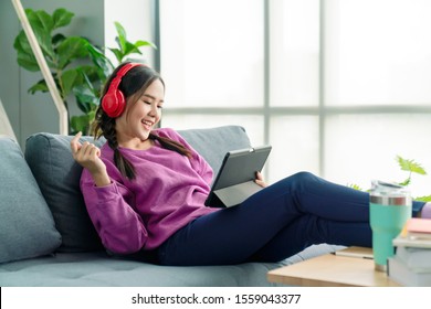 Candid of asian woman using tablet for watching online movie stream mobile device on sofa at living room. Young happy girl enjoying with entertainment media online on weekend. - Powered by Shutterstock