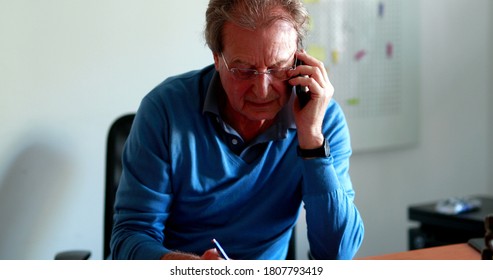 Candid Business Man Working And Talking On Cellphone While Taking Notes. Casual Real Life Older Person Speaking On Phone