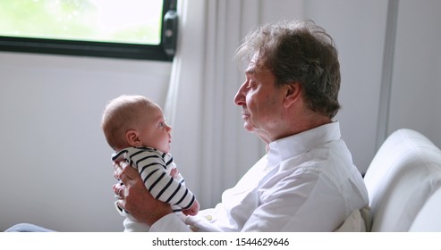 Candid Grand-father Holding Newborn Grand-son Baby In Sofa Indoors Authentic Grandpa Interaction