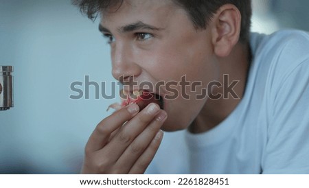 Candid handsome young adolescent boy eating fruit closeup face. Kid eats healthy snack portrait