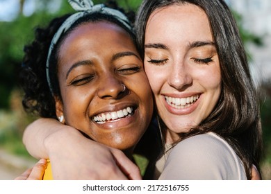 Candid happy multiracial best women friends embracing outdoors - Close up view of two diverse girls hugging each other with closed eyes smiling - Female friendship