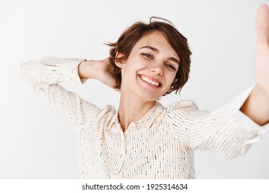 Candid happy woman posing for selfie, holding smartphone and taking pic of herself with cheerful smile, standing carefree on white background. - Shutterstock ID 1925314634