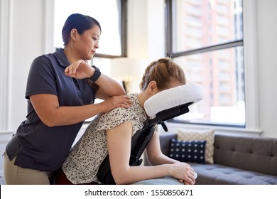 Candid image of an attractive employee getting a chair massage during a appointment with a professional asian physiotherapist in a design kinesio clinic
