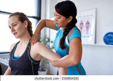 Candid image of an attractive patient during a appointment with professional asian physiotherapist in design kinesio clinic working and massaging her neck and shoulder pain