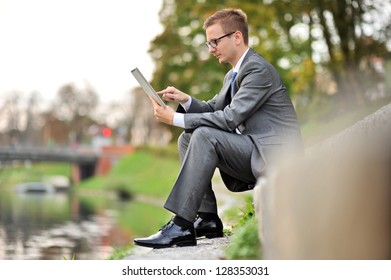 Candid image of young businessman sits using Tablet Computer near the river