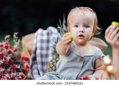 Candid Lifestyle Portrait Of Caucasian Baby Girl One Year Old Eating Healthy Food On Picnic Blanket At Summer On Backyard In Suburb