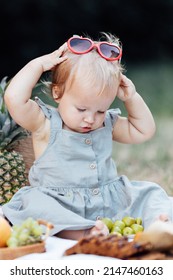 Candid Lifestyle Portrait Of Caucasian Baby Girl One Year Old Eating Healthy Food On Picnic Blanket At Summer On Backyard In Suburb