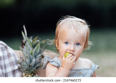 Candid Lifestyle Portrait Of Caucasian Baby Girl One Year Old Eating Healthy Food On Picnic Blanket At Summer On Backyard In Suburb