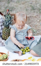 Candid Lifestyle Portrait Of Caucasian Baby Girl One Year Old Eating Healthy Food On Picnic Blanket At Summer On Backyard In Suburb