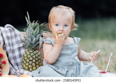 Candid Lifestyle Portrait Of Caucasian Baby Girl One Year Old Eating Healthy Food On Picnic Blanket At Summer On Backyard In Suburb