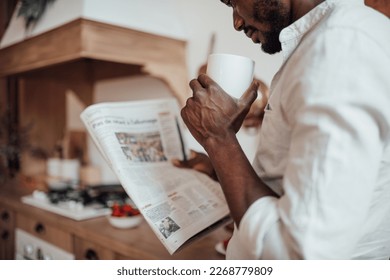 Candid millennial authentic diverse portrait of african american man relax time in neutrals tones kitchen. Brown skin male drink tea at breakfast domestic life and morning routine reading newspaper - Powered by Shutterstock