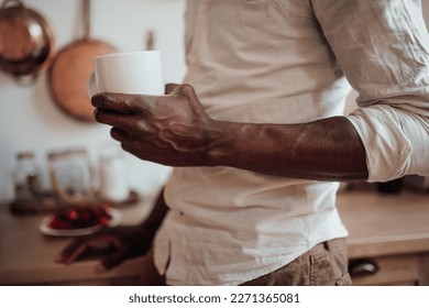 Candid millennial authentic diverse portrait of african american man relax time in neutrals tones kitchen. Brown skin male drink tea at breakfast domestic life and morning routine in natural lighting - Powered by Shutterstock