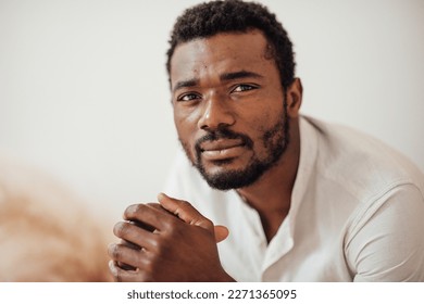 Candid millennial authentic diverse portrait of african american man relax time at apartment in neutrals tones interior.Domestic life multi ethnic male having thoughtful facial expression in day light