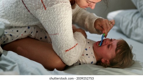 Candid Mother Brushing Crying Baby Teeh. Upset Infant Boy Not Wanting To Brush Teeth