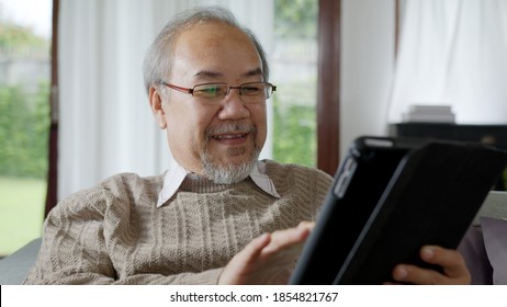 Candid Of Old Asian Retired Man Using Tablet Computer To Transfer Money Online Or Financial Payment And Read Text, Smile Or Laugh With Happy And Positive. Senior Asian With Digital Technology Concept