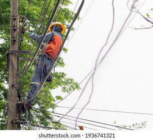 Candid Photo Of Brave Man Working In The Sun On Dangerous Job. Electrician Wears Hard Hat Helmet And Safety Tools Climb Electric Pole To Maintenance Parts And Power Cable.  Copy Space.