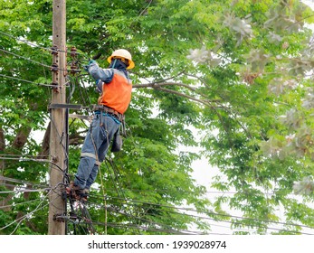 Candid Photo Of Brave Man Working In The Sun On Dangerous Job. Electrician Wears Hard Hat Helmet And Safety Tools Climb Electric Pole To Maintenance Parts And Power Cable. 