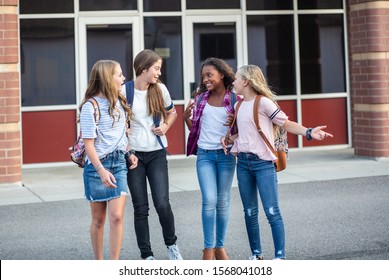 Candid photo of a group of teenage girls socializing, laughing and talking together at school. A multi-ethnic group of real junior high aged students walking outside a school building