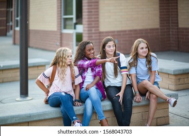 Candid Photo Of A Group Of Teenage Girls Socializing, Laughing And Talking Together At School. A Multi-ethnic Group Of Real Junior High Aged Students Sitting Outside A School Building