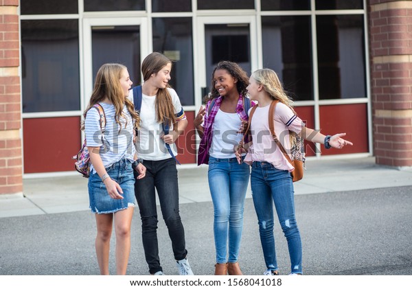 Candid photo\
of a group of teenage girls socializing, laughing and talking\
together at school. A multi-ethnic group of real junior high aged\
students walking outside a school\
building