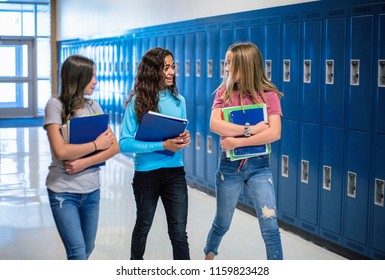 Candid photo of Three Junior High school Students talking together in a school hallway. Diverse Female school girls smiling and having fun together during a break at school