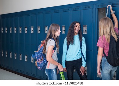 Candid photo of Three Junior High school Students talking together in a school hallway. Diverse Female school girls smiling and having fun together during a break at school standing by their lockers