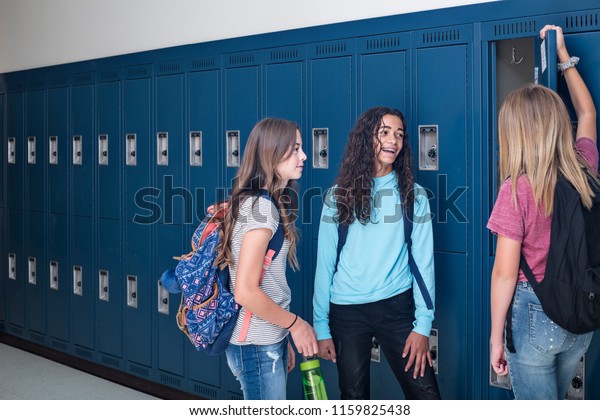 Candid photo of Three Junior High school Students\
talking together in a school hallway. Diverse Female school girls\
smiling and having fun together during a break at school standing\
by their lockers
