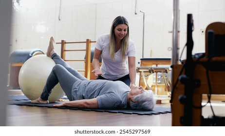 Candid Pilates Coach helping an elderly woman to exercise and stretch body at physiotherapist studio session - Powered by Shutterstock