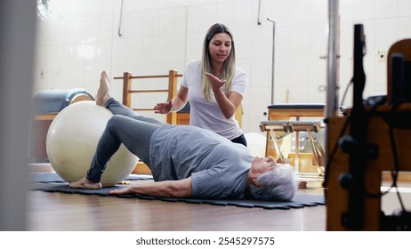 Candid Pilates Coach helping an elderly woman to exercise and stretch body at physiotherapist studio session - Powered by Shutterstock