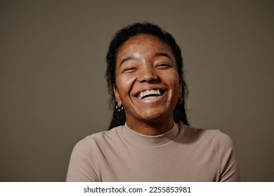 Candid portrait of black young woman laughing against neutral beige background in studio focus on skin texture - Powered by Shutterstock