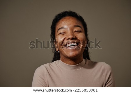 Candid portrait of black young woman laughing against neutral beige background in studio focus on skin texture