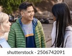 Candid portrait of a cheerful young Asian man laughing with his diverse group of friends in an outdoor setting. Young adults authentic representation of multicultural friendship and social interaction