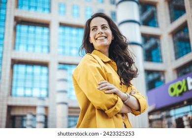 Candid portrait of a cheerful young woman wearing an yellow shirt spending time in the city. The pretty female has a joyful expression. Successful proud woman in city street at sunset - Powered by Shutterstock