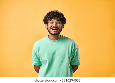 Candid portrait of a handsome curly-haired young man in a turquoise t-shirt and glasses on a yellow background laughing. - Powered by Shutterstock