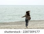 Candid portrait of a strong independent carefree woman with flowing hair against the background of the sea in autumn.