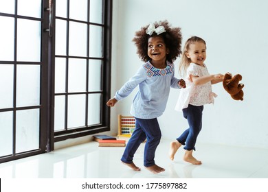 Candid Portrait Of Two Energetic Playful Young Diverse Friends Children Playing Indoors. African American And Caucasian Girls Together