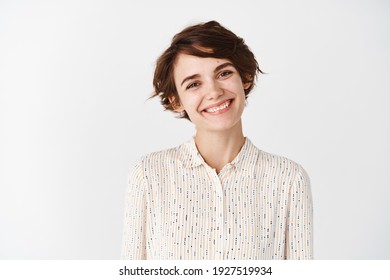 Candid portrait of young beautiful woman smiling happy at camera, looking friendly, standing on white background.