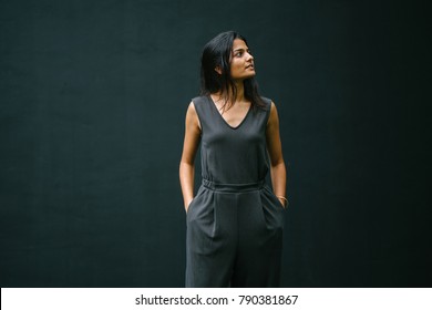 Candid Portrait Of A Young Woman Smiling Against A Plain Dark Background. The Young Indian Lady Is Attractive And Dressed Professionally And Is Confident, Calm And Relaxed. She Is Looking Away.