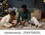 Candid scene of happy African American family of father and son playing with toy railroad together on Christmas morning