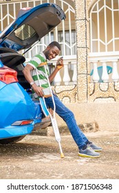 Candid Shot Of African Man, With A Crutch In The Arm, Holding Phone At The Back Of An Opened Car Booth- Lifestyle Concept