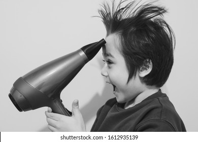 Candid Shot, Cute Kid Drying His Hair With Hair Dryer, Cheerful 6 Years Old Boy Try To Making His Hair Like A Crazy Expression, Flying Hair, Lightness And Happiness. Concept Child Care Concept