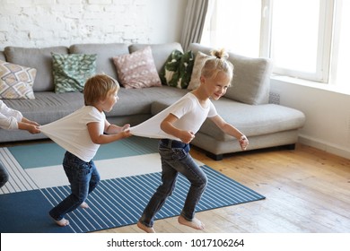 Candid Shot Of Emotional Caucasian Children Siblings Doing Conga Or Dancing Barefooted At Home, Playing Indoor Games On Rainy Cold Weather, Having Happy Excited Facial Expressions. Joy And Fun