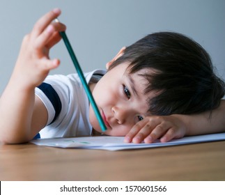 Candid Shot Of Kid Boy Holding Colour Pencil Sitting Alone With Bored Face, Preschool Child Boy Laying Head Down On Table With Deep In Throught, Five Years Old Kid Bored With School Homework