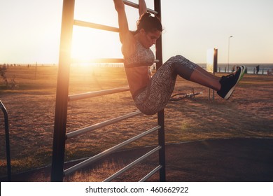 Candid shot of real healthy and fit woman performing hanging leg raises on outdoor fitness station in sunset at beach promenade. Showing strong abdominal six-pack.