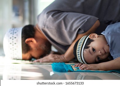 Candid shot of Religious Asian Muslim Man teaching his little son to pray to God in Sujud position.For praise and glorify Allah.Little boy looking to the camera.Concept of Muslim people.