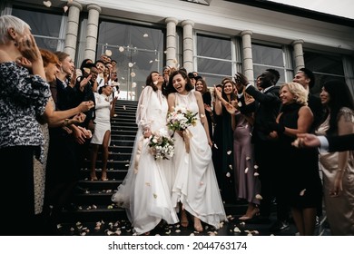 Candid shot of two female lesbian LGBT brides walking down the stairs during their wedding ceremony as guests throwing rose petal