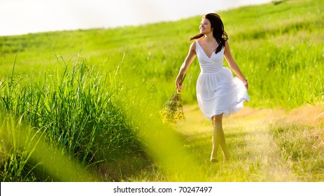 Candid skipping carefree adorable woman in field with flowers at summer sunset.