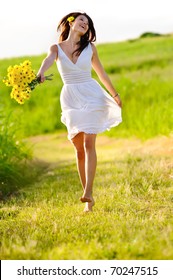 Candid Skipping Carefree Adorable Woman In Field With Flowers At Summer Sunset.