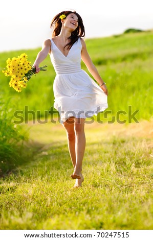 Candid skipping carefree adorable woman in field with flowers at summer sunset.